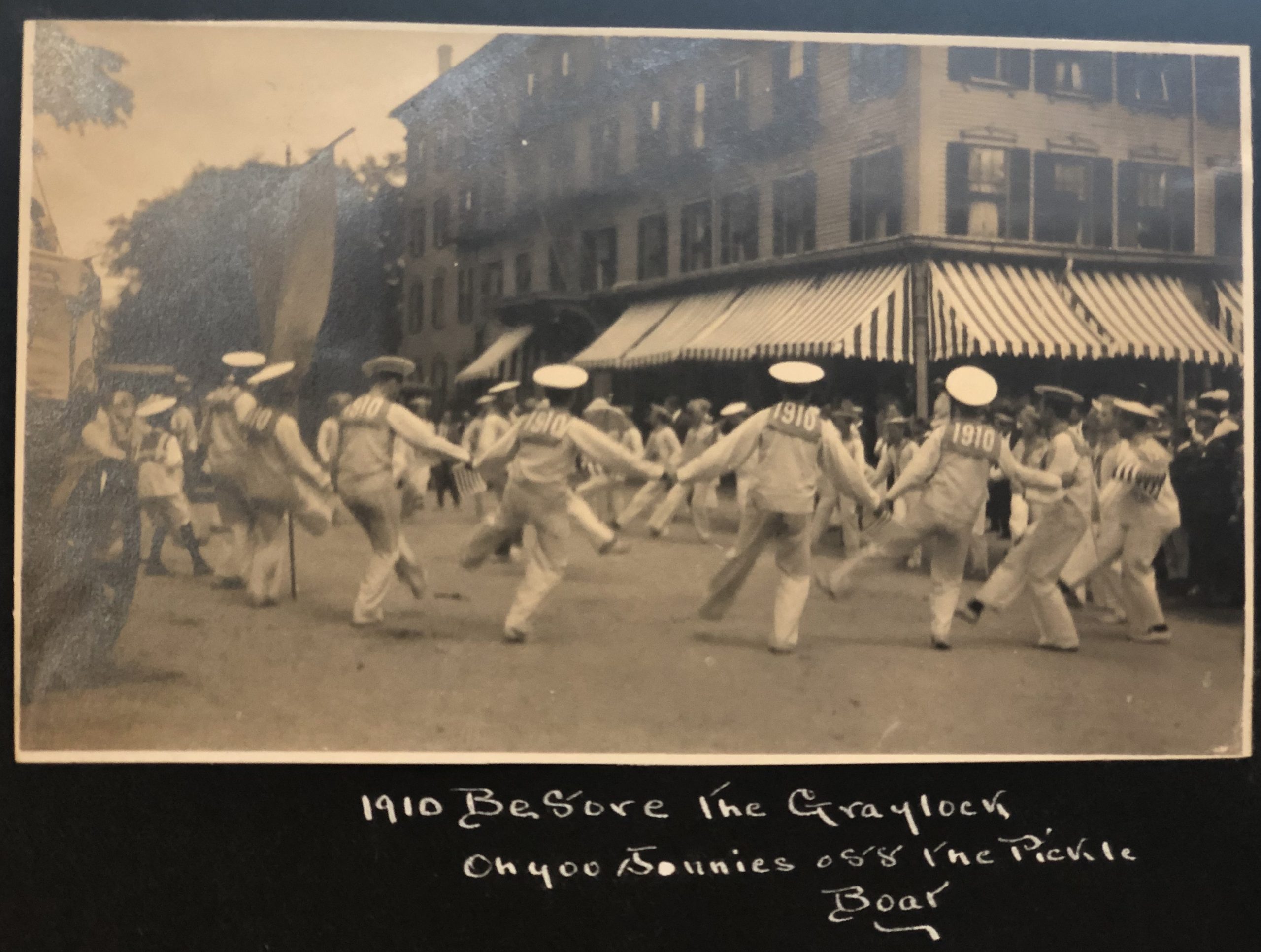 A black and white photograph in an album shows men from the class of 1910 dressed as sailors with dancing in the street at their three-year reunion.